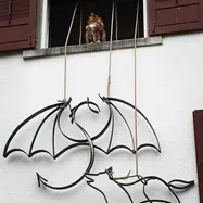 Ein Metalldrache und ein Metallwolf werden an einer Hauswand montiert. Auf dem Fenstersims sitzt eine Katze